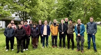 Group of people outdoors in a grassy area with trees, faces blurred.